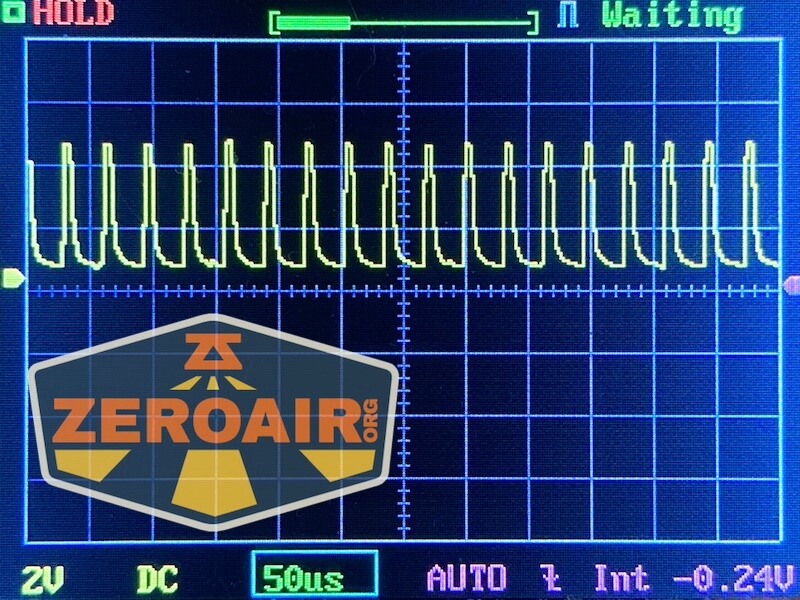 An oscilloscope screen displays a repeating waveform with sharp peaks and valleys. The settings at the bottom read “2V DC 50us AUTO.” A semi-transparent ZeroAir.org logo covers the lower left corner.