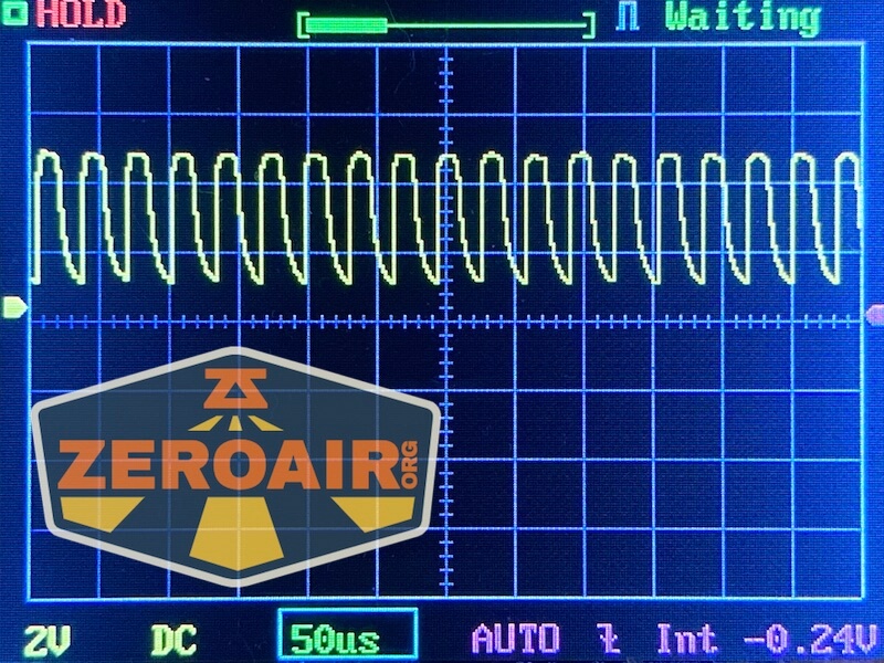 A digital oscilloscope screen shows a repeating waveform signal. Displayed settings include 2V DC vertical scale, 50 microseconds horizontal scale, and an AUTO trigger mode. A ZeroAir.org logo is overlaid on the image.