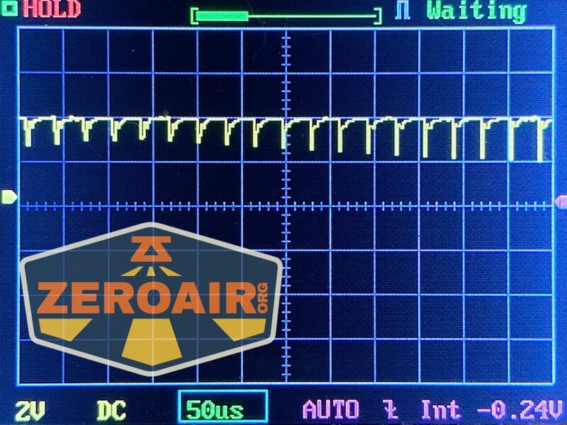 An oscilloscope screen displays a repeating waveform with sharp downward spikes. The settings at the bottom show 2V, DC, 50 microseconds per division, and AUTO mode. The ZeroAir.org logo is overlaid.