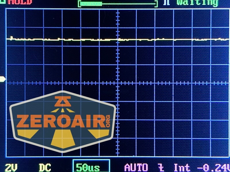 A digital oscilloscope screen displays a flat, yellow waveform near the top with a grid background. The screen shows 50µs and 2V DC at the bottom. A semi-transparent ZeroAir.org logo is overlaid.