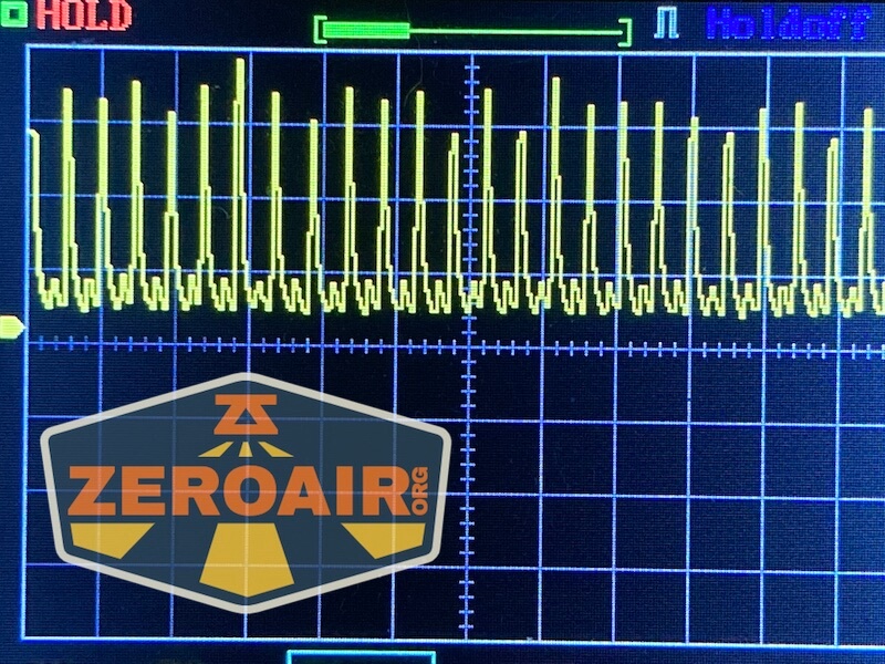 An oscilloscope screen displays a repeating spiked waveform. The words ZEROAIR.ORG appear at the bottom left within a shield-shaped logo. The screen shows grid lines and measurement markers.