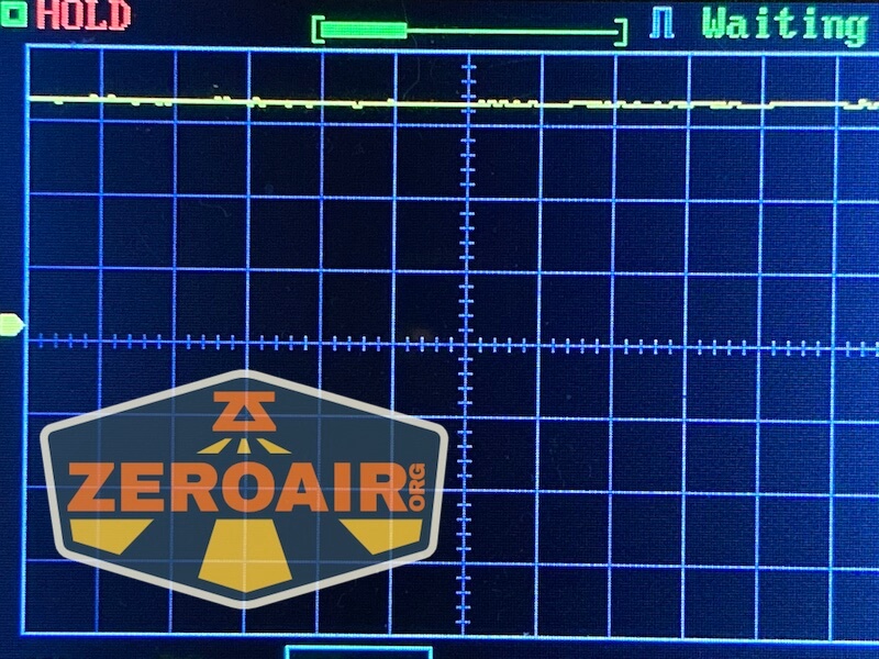 A digital oscilloscope screen showing a mostly flat yellow waveform near the top, with grid lines and text reading HOLD and Waiting. A ZEROAIR.org logo is partially visible in the lower left corner.
