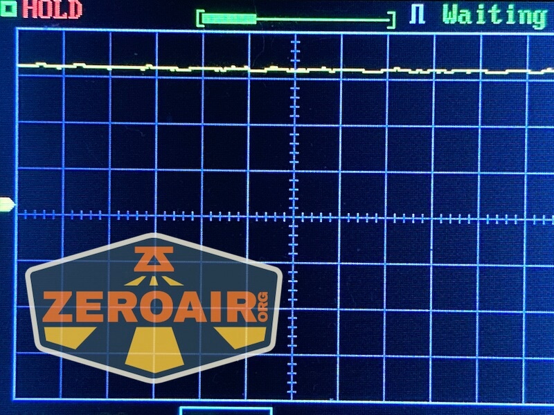 A digital oscilloscope screen displaying a mostly flat yellow waveform with minor fluctuations. The words “HOLD” and “Waiting” appear at the top, and a badge labeled ZEROAIR.ORG is visible in the bottom left corner.
