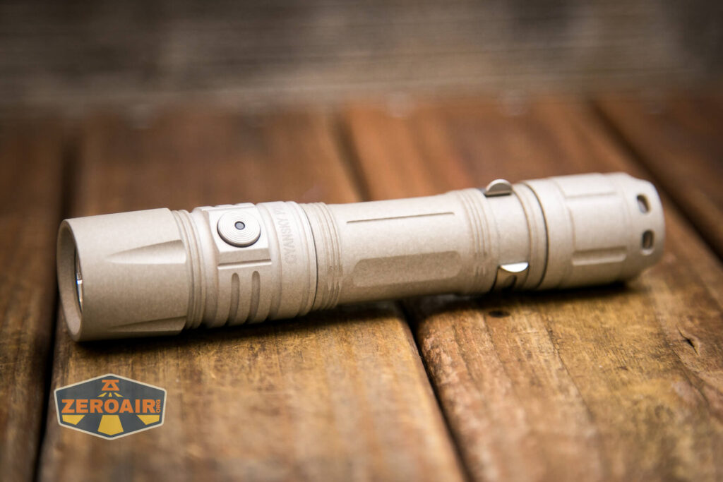 A tan-colored tactical flashlight with a side button and metal clip rests on a wooden surface. A logo reading ZeroAir appears in the bottom left corner.