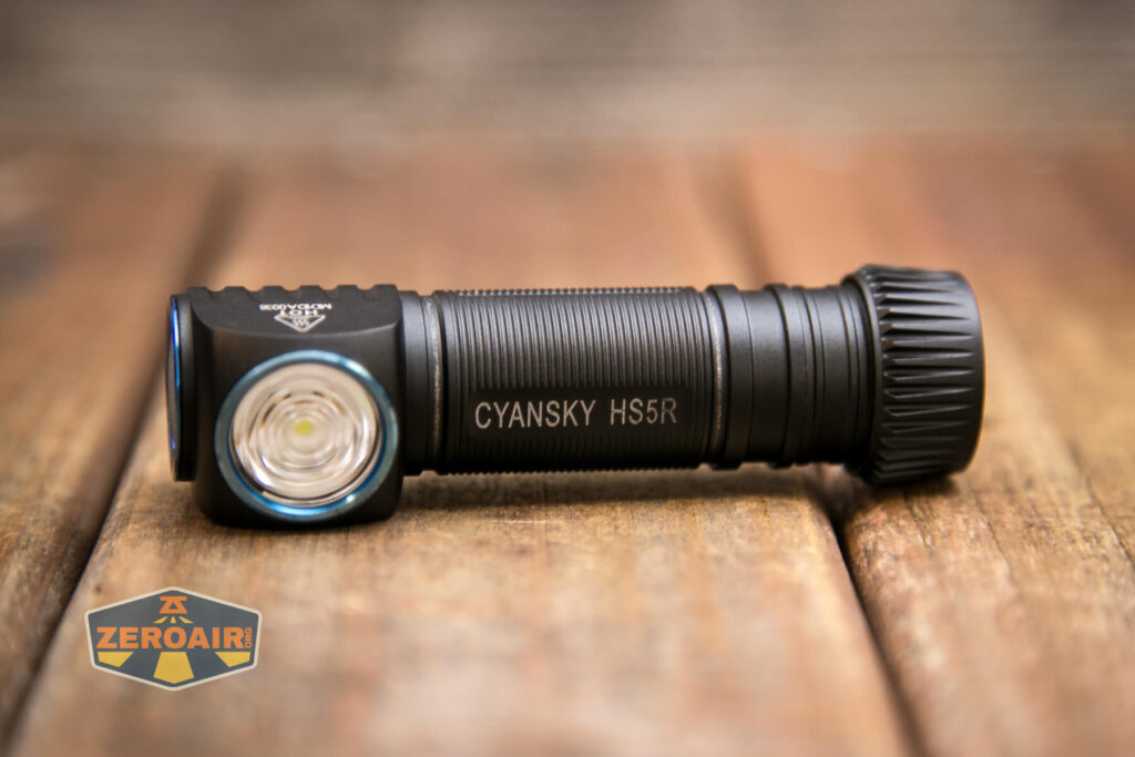 A black Cyansky H5R flashlight with a side-mounted lens is lying on a wooden surface. The flashlight has ribbed grip details, and a ZEROAIR logo is visible in the bottom left corner.