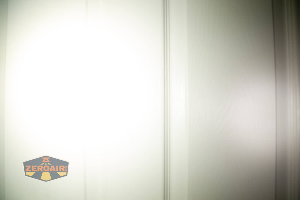 A bright flashlight beam illuminates the center of a white paneled door, causing overexposure. The ZeroAir logo appears in the lower left corner of the image.