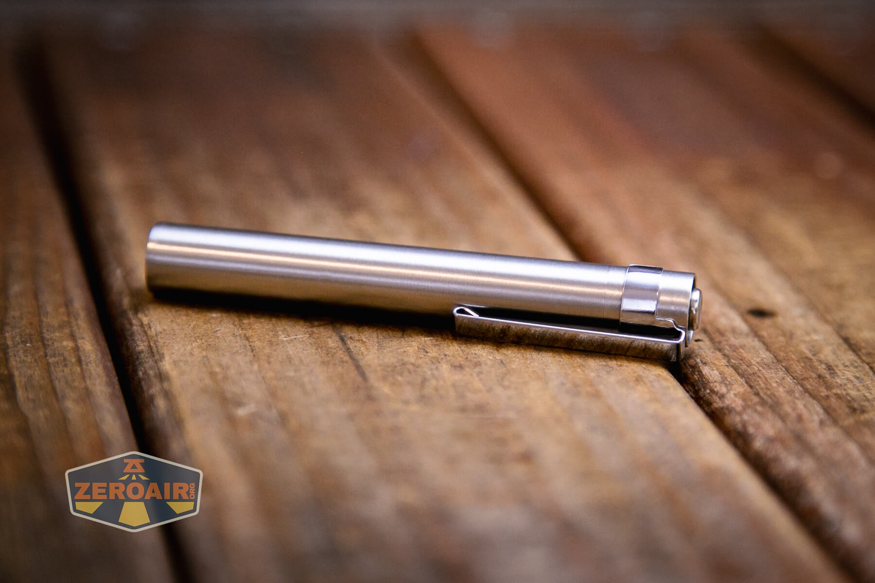 A slim, metallic pen-shaped object with a clip lies on a wooden surface. The BLF-348, available at KillzoneFlashlights.com, is featured as the ZeroAir logo appears in the lower left corner of the image.