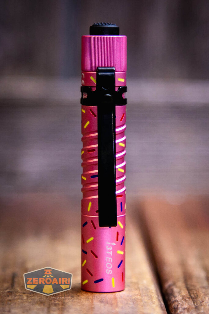 A pink flashlight with a black clip stands upright on a wooden surface. The flashlight has a pattern of colorful sprinkles and the model name I3T EOS printed on it. The ZeroAir logo is visible in the lower left corner.
