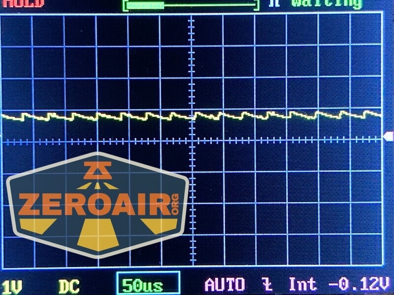 An oscilloscope screen shows a yellow waveform with slight fluctuations. The horizontal axis is set to 50 microseconds per division, and the vertical axis is set to 1V per division. A ZeroAir.org logo overlays the image.