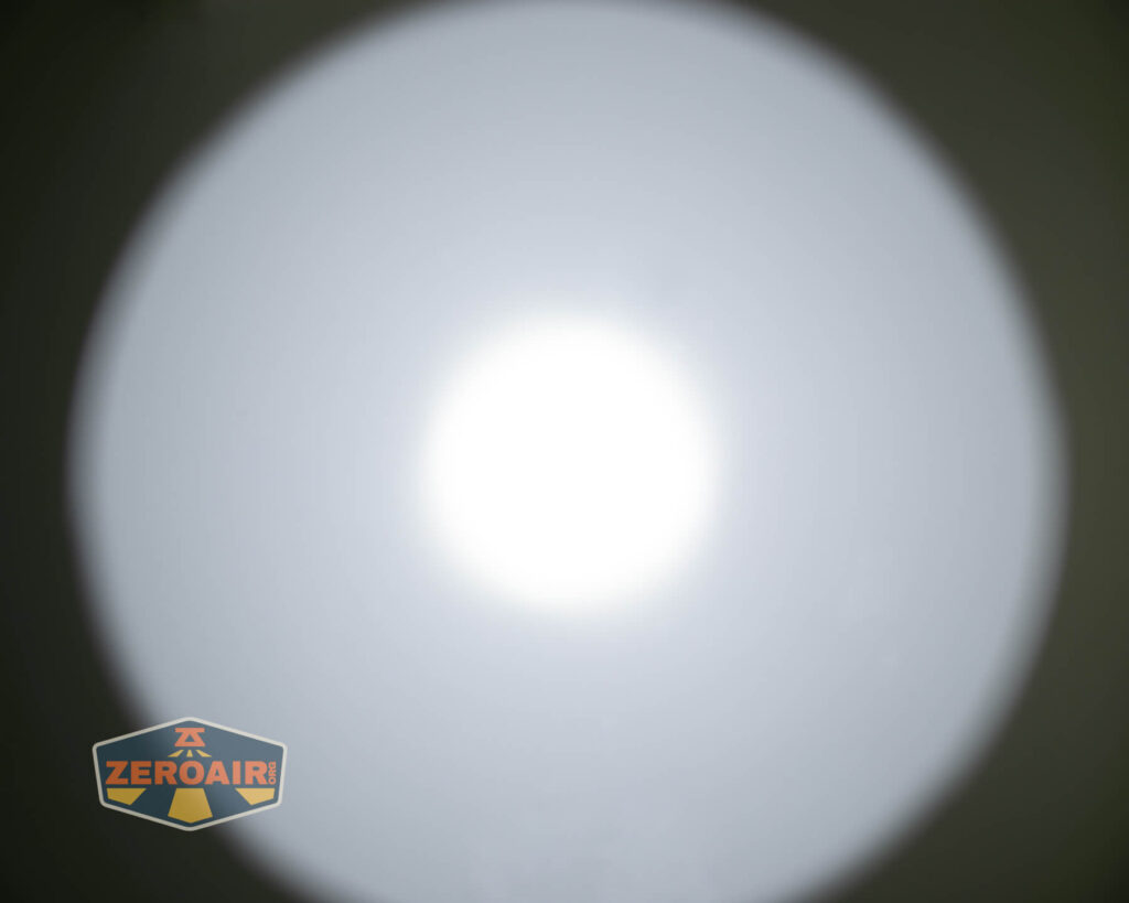 A circular white spotlight beam is centered on a dark background. The bottom left corner shows a logo with the text ZEROAIR! on a shield-shaped emblem.