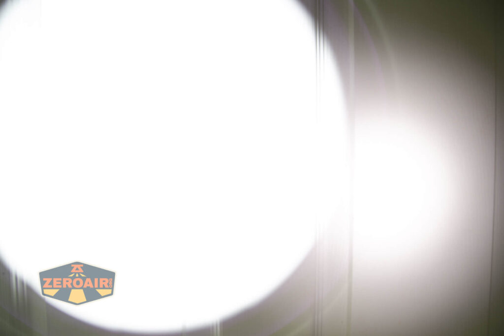 A large, bright white circular light dominates the center of the image, creating a strong glare and partially obscuring a background with faint vertical lines. A ZEROAIR! logo is visible in the lower left corner.