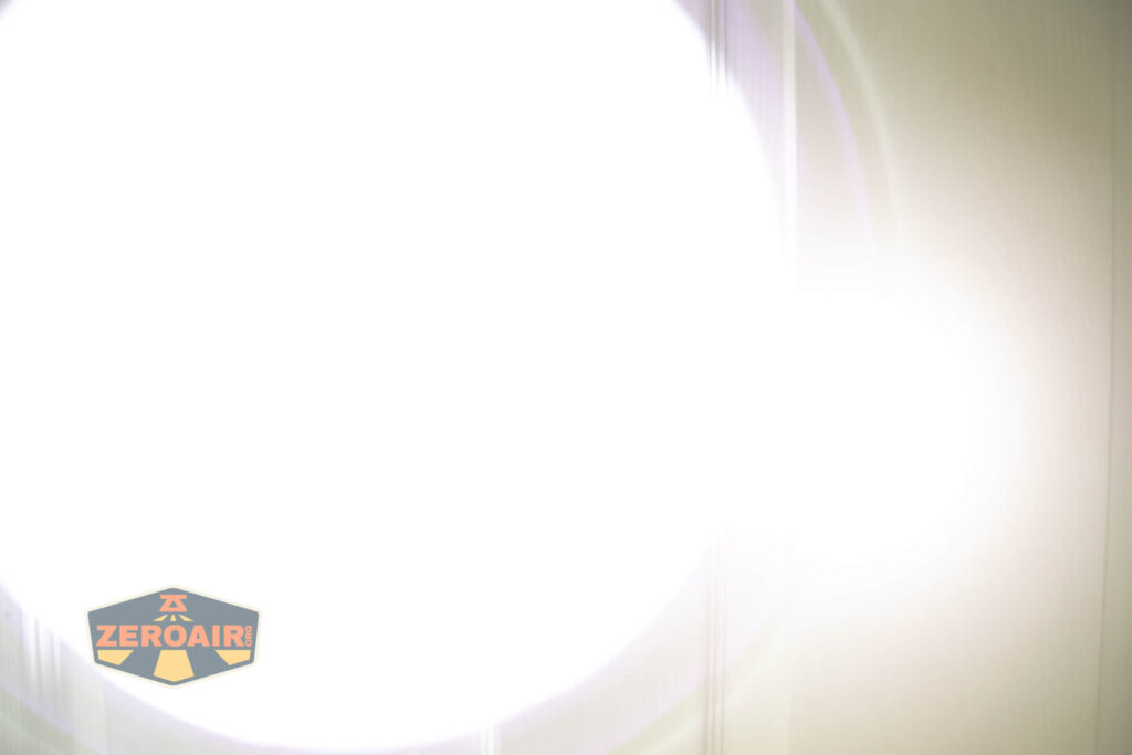 A bright, white circular light dominates the center of the image, causing overexposure. The background is barely visible. In the lower left corner, there is a logo that reads ZEROAIR! on a dark, shield-shaped background.