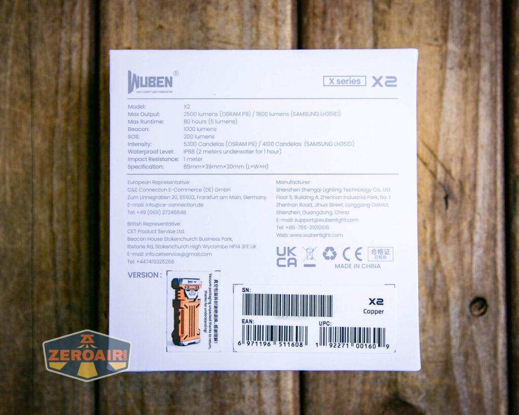 The back of a Wuben X2 flashlight box displays technical specifications, certifications, a barcode, serial numbers, and manufacturer details. The box is placed on a wooden surface. A Zeroair logo is in the lower left corner.