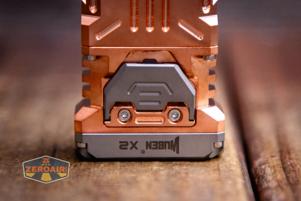 Close-up of the base of a copper and gray Wuben X2 flashlight resting on a wooden surface, with the ZeroAir logo visible in the bottom left corner of the image.