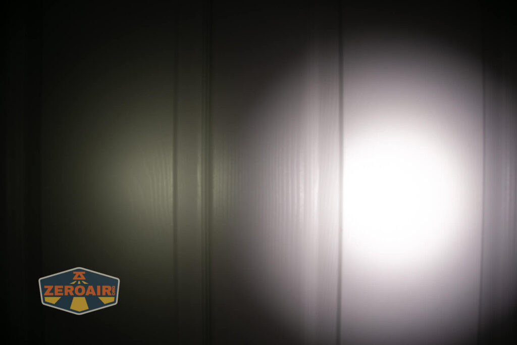 A round beam of white light is projected onto a vertical surface, creating a bright spot in the center with a dimmer area around it; a ZeroAir logo is in the lower left corner.