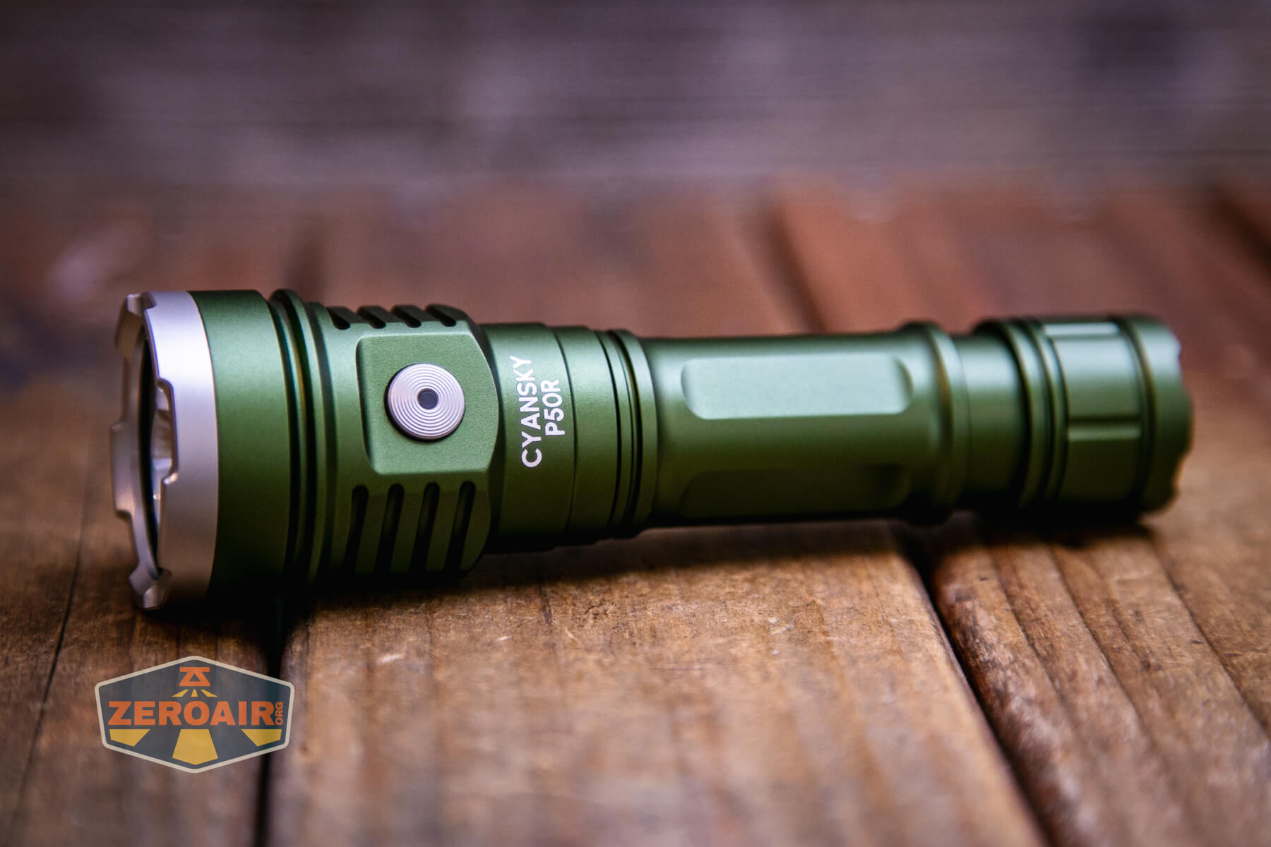 A green Cyansky P50R flashlight lies on a wooden surface, featuring a silver button and ridged edges. The Cyansky P50R flashlight model and brand are printed on its side, with the ZeroAir logo in the bottom left corner.