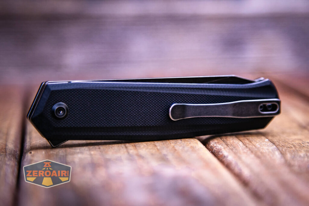 A closed black Kansept Integra Flipper Knife with a metal clip rests on a wooden surface. The knife features a modern design, and the image has a shallow depth of field. A ZeroAir logo is in the bottom left corner.