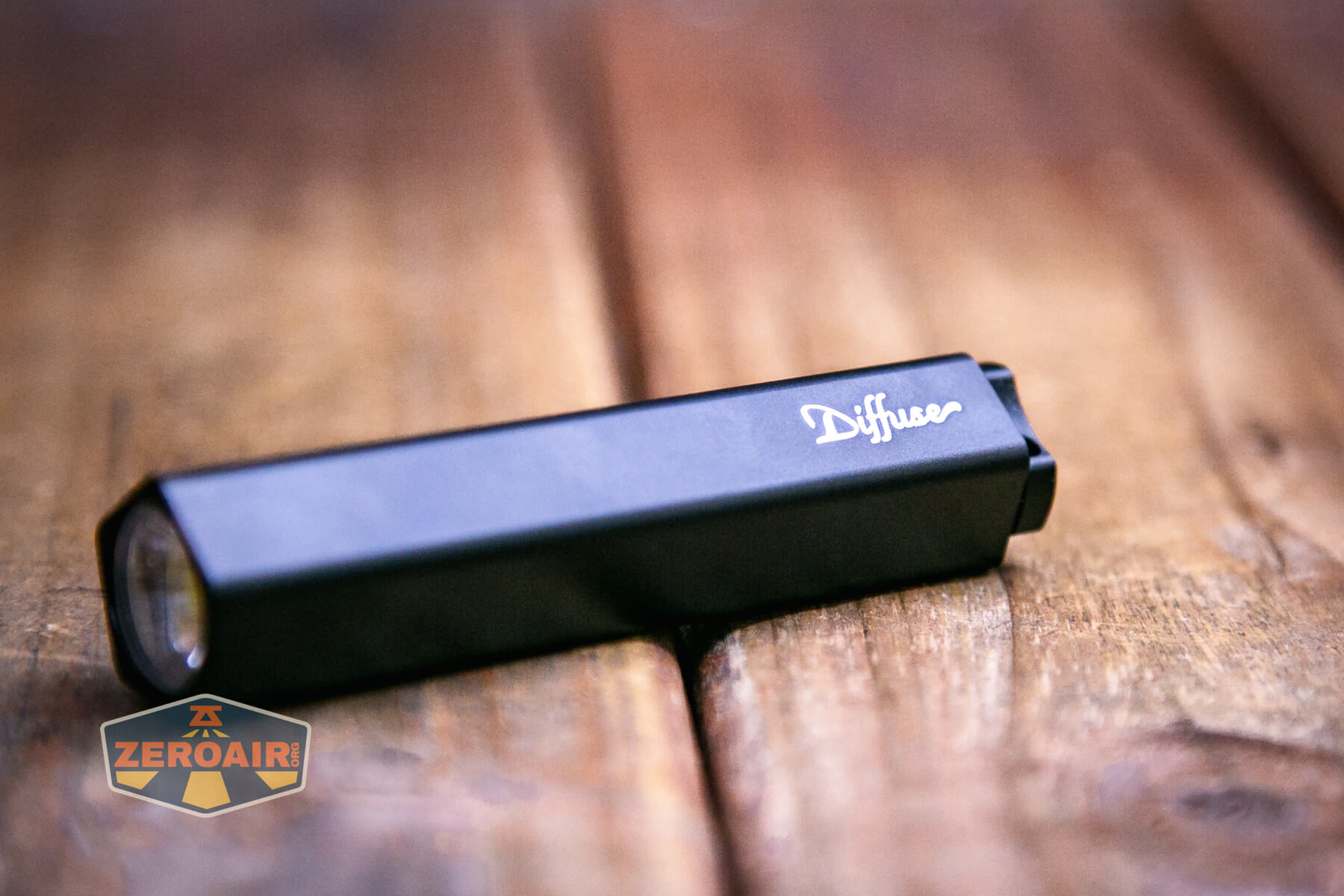 A black, rectangular Olight Diffuse 14500 EDC Flashlight lies on a wooden surface. The ZeroAir logo is visible in the lower left corner of the image.
