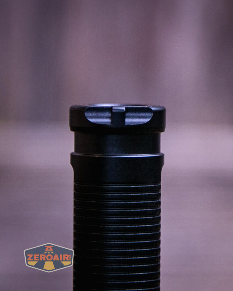 A close-up of the top section of a black cylindrical flashlight with a textured grip. The background is blurred, and a ZeroAir logo appears in the bottom left corner.