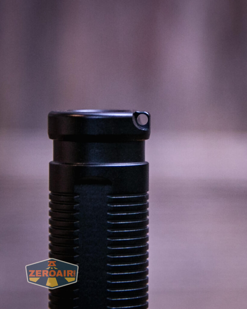 A close-up view of the top section of a black, ribbed cylindrical object, possibly a flashlight, with a small hole near the top edge. The background is blurred, and a “ZEROAIR” watermark is present in the lower left corner.