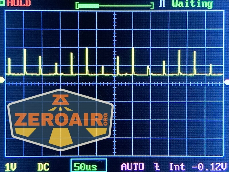 An oscilloscope screen displays a fluctuating yellow waveform with various peaks and troughs. The RovyVon E30 Pro MAO flashlight rests nearby, while the ZEROAIR.org logo appears in the foreground. Settings include 1V, 50µs, DC, AUTO, and a -0.12V baseline.