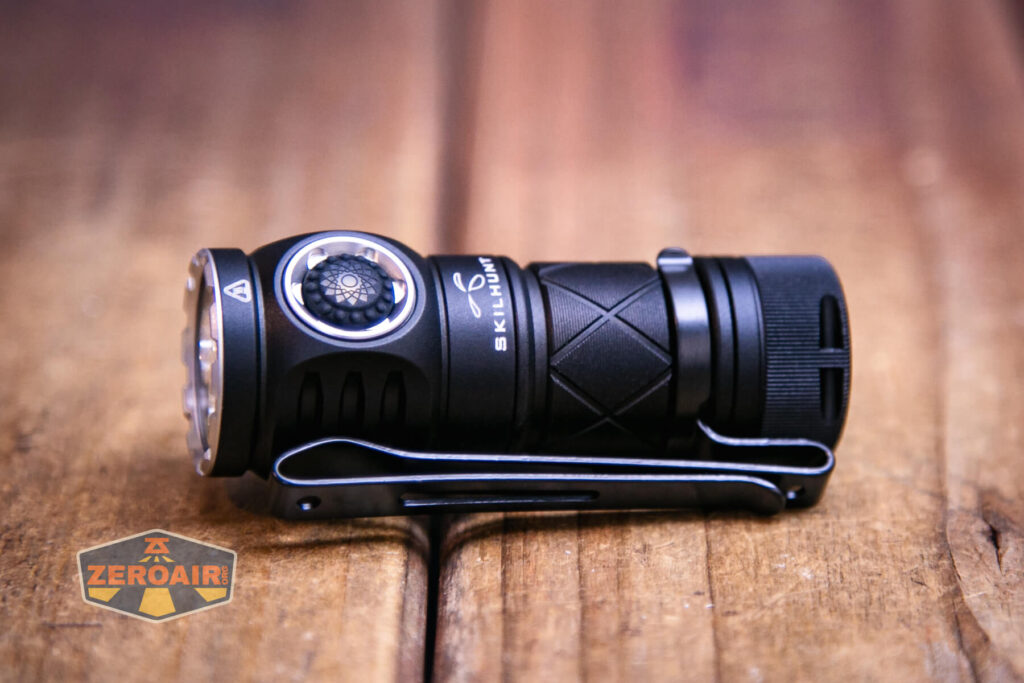 A compact black Skilhunt EC200S-Red Mini EDC flashlight with a metal clip lies on a wooden surface. It features a large side button and SKILHUNT branding on the body. The ZeroAir logo appears in the bottom left corner.