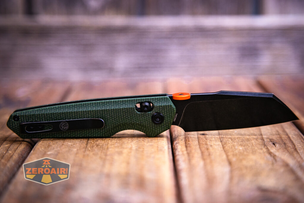 A Vosteed Talarurus micarta knife with a green textured handle and black tanto blade rests on a wooden surface. The knife features an orange thumb stud, black pocket clip, and a visible ZEROAIR logo in the lower left corner.