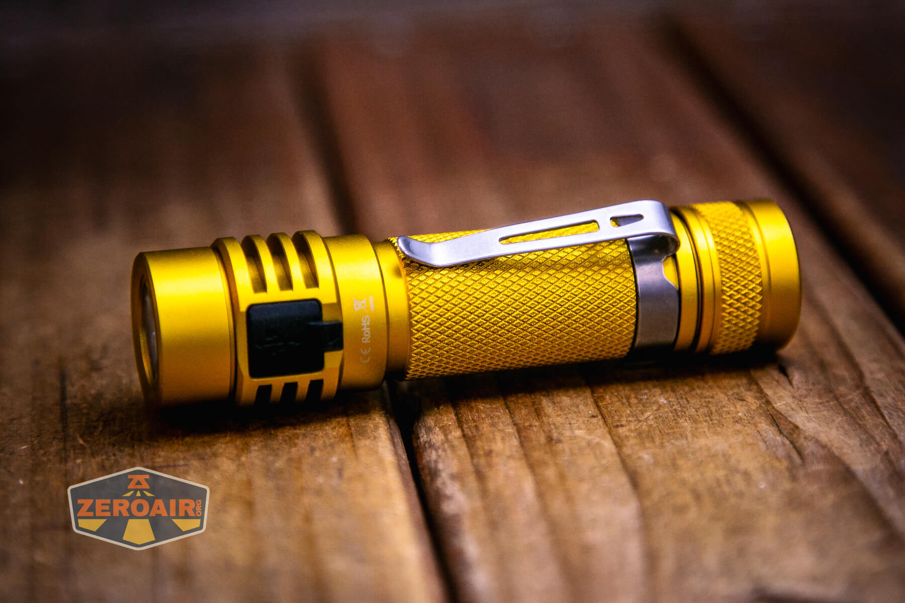 A yellow Wurkkos Golden WK03 Flashlight with a textured grip and silver pocket clip rests on a wooden surface. The ZeroAir logo appears in the bottom left corner of the image.