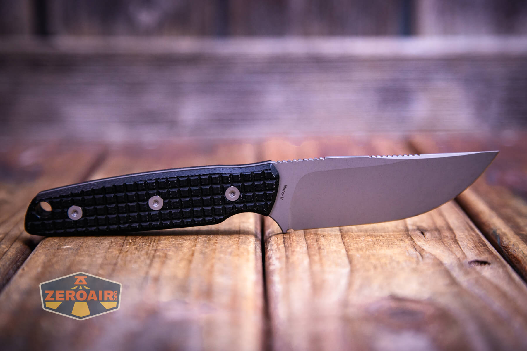 A Vosteed Mink Fixed-Blade Knife with a textured black handle and silver blade rests on a wooden surface. The ZeroAir logo appears in the lower left corner of the image.