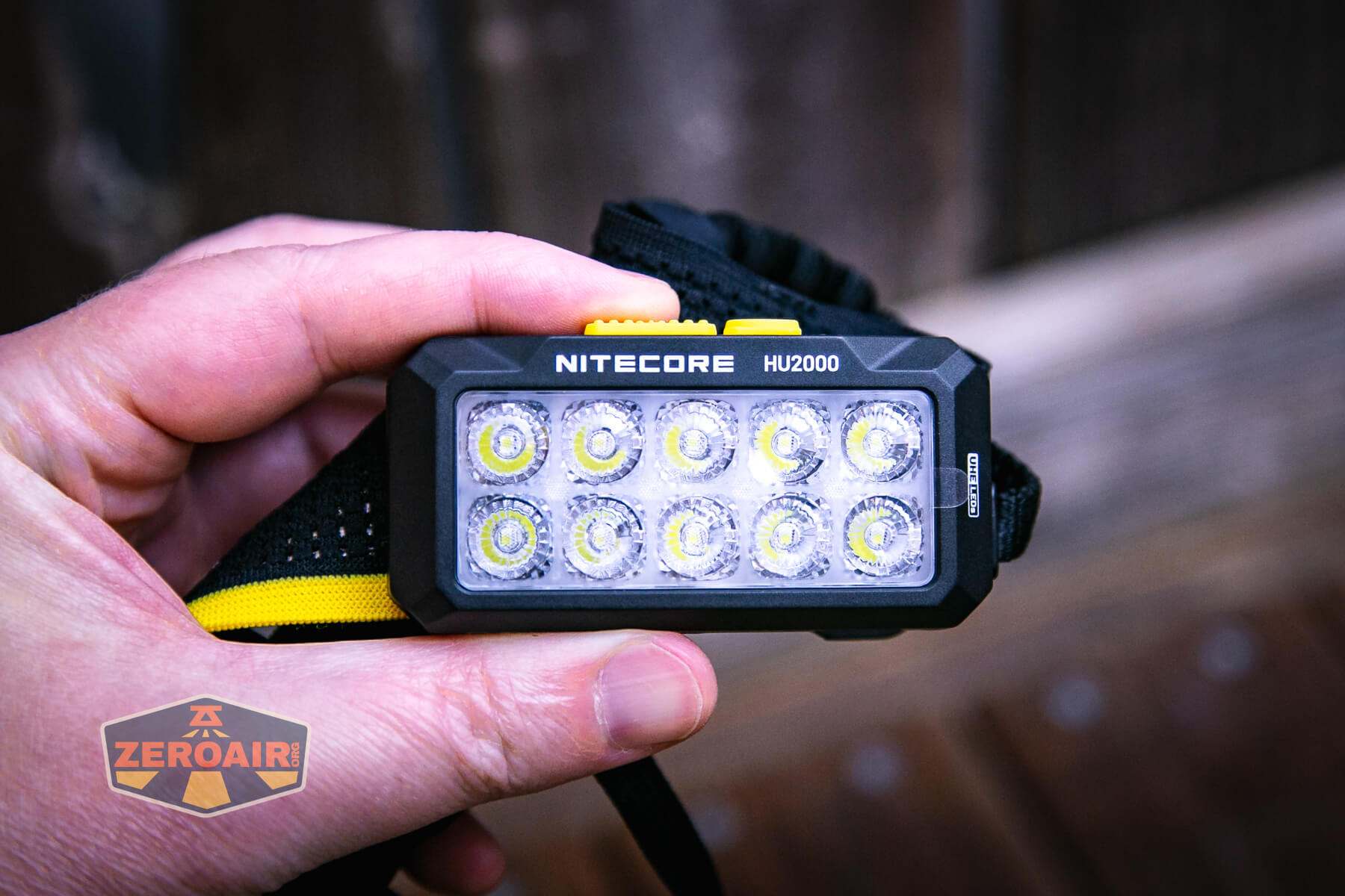A hand holds the Nitecore HU2000 headlamp, which features twelve LED lights on its front. The device is black with yellow accents, and the ZeroAir logo appears in the lower left corner of the image.