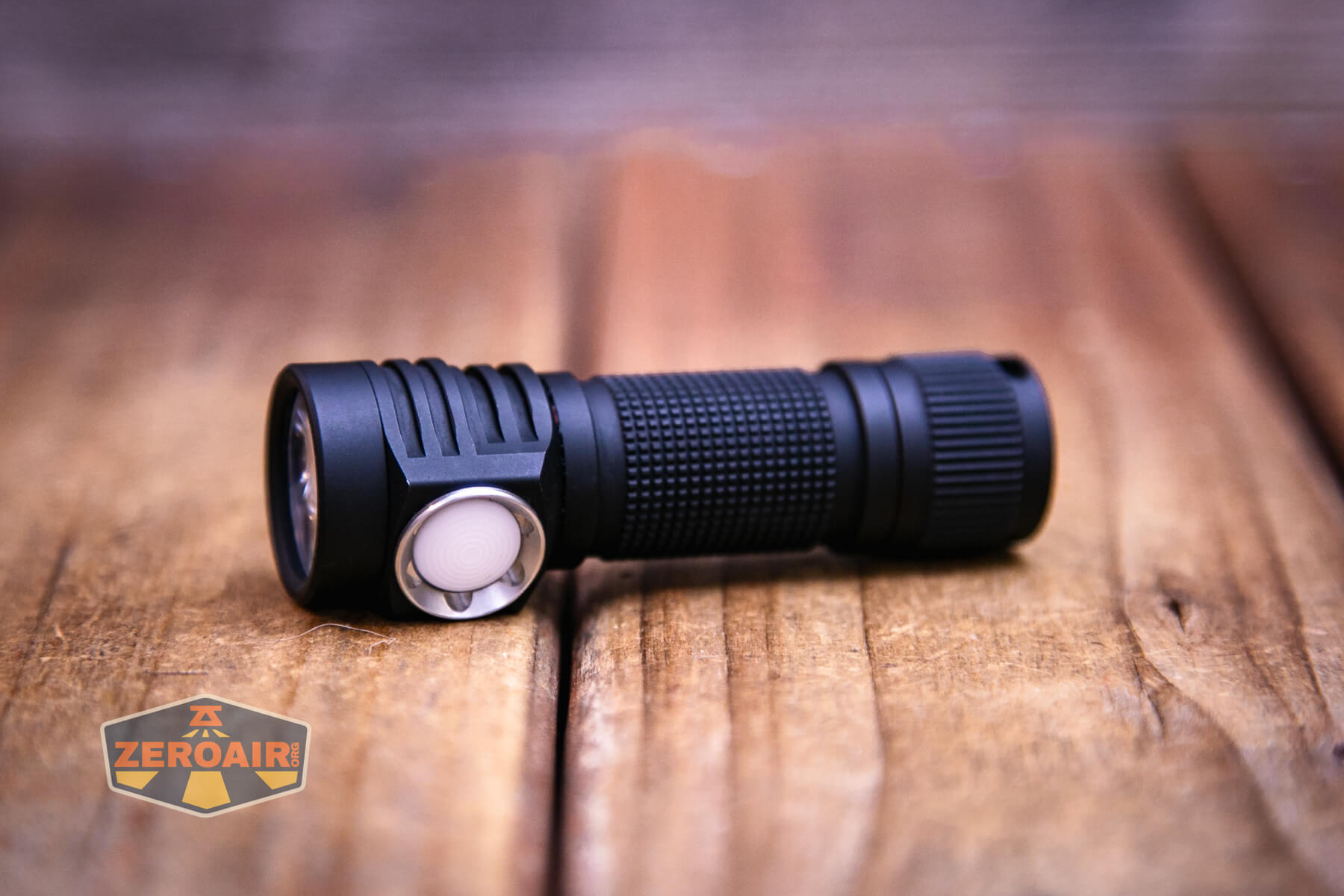 A black Emisar D3AA 4500K flashlight with a textured grip and a white side button rests on a wooden surface. A logo with the text “ZEROAIR” is visible in the bottom left corner.