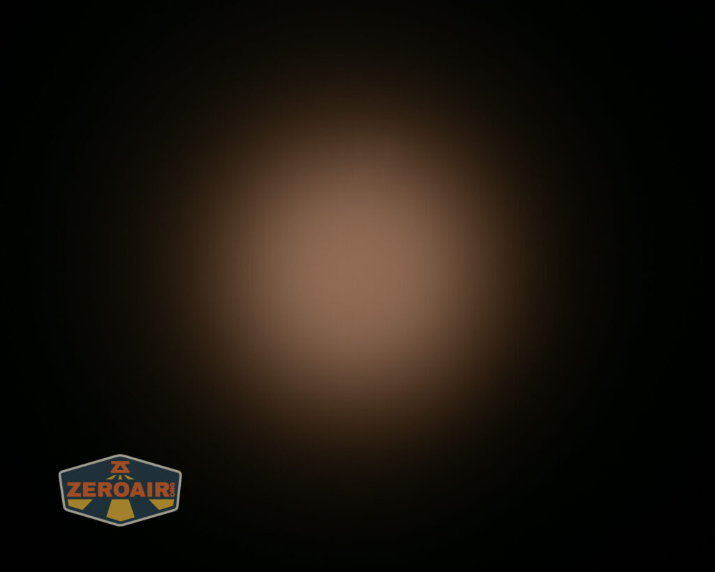 A soft, circular beam of warm light is centered on a dark background. In the lower left corner, there is a small logo with the text ZEROAIR in orange and yellow.