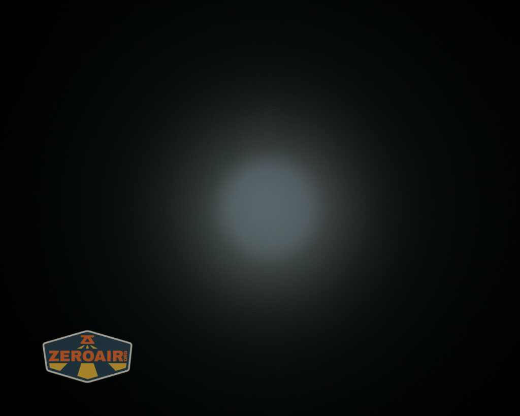 A circular white light beam shines in the center of a black background. The beam is surrounded by a faint halo. A shield-shaped logo with the text ZEROAIR appears in the lower left corner.