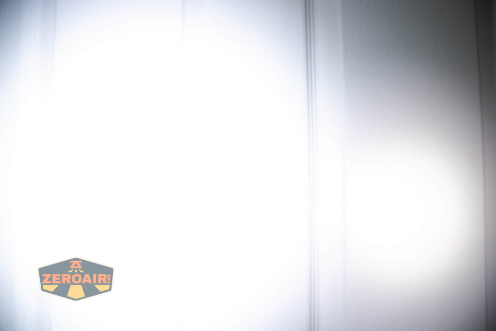 A bright white light is shining on a paneled surface, likely a door or wall, creating a glare and obscuring most details. A logo reading ZEROAIR appears in the lower left corner.