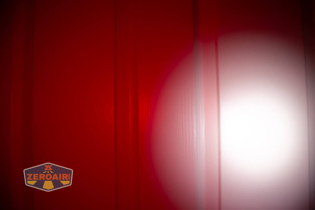 A bright white spotlight shines on a red textured surface, creating a circular highlight. The ZeroAir logo is in the bottom left corner.