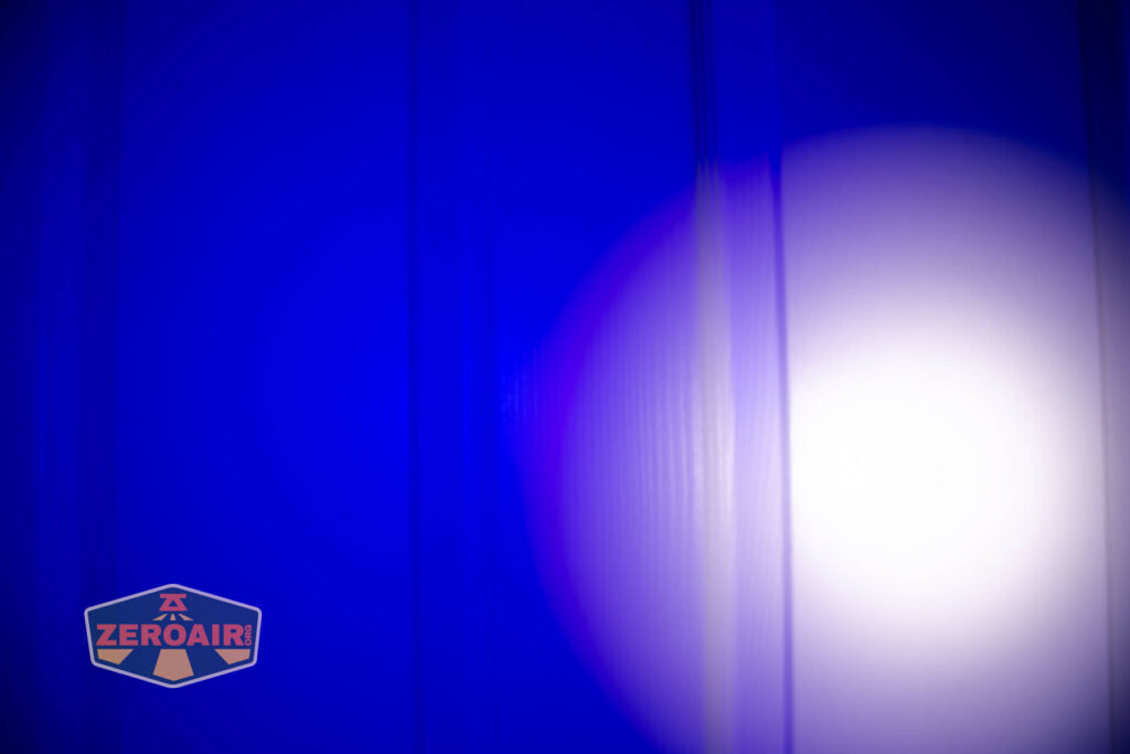 A circular white spotlight appears on a blue vertical surface with visible lines. The ZeroAir logo is in the bottom left corner of the image.