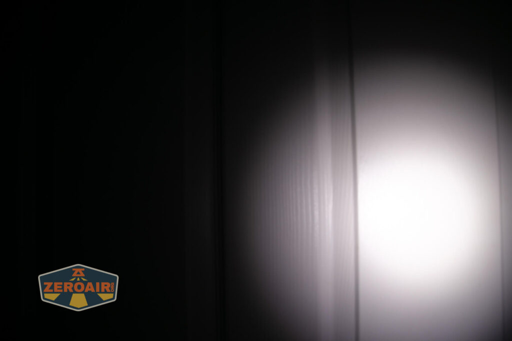 A beam of white light from a flashlight illuminates a section of a vertical, textured white wall in a dark room. The Zeroair logo appears in the lower left corner.