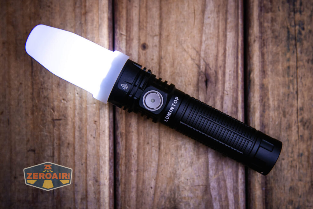 A black Lumintop flashlight with a white diffuser cap is turned on and placed on a wooden surface. The ZeroAir logo is visible in the bottom left corner of the image.