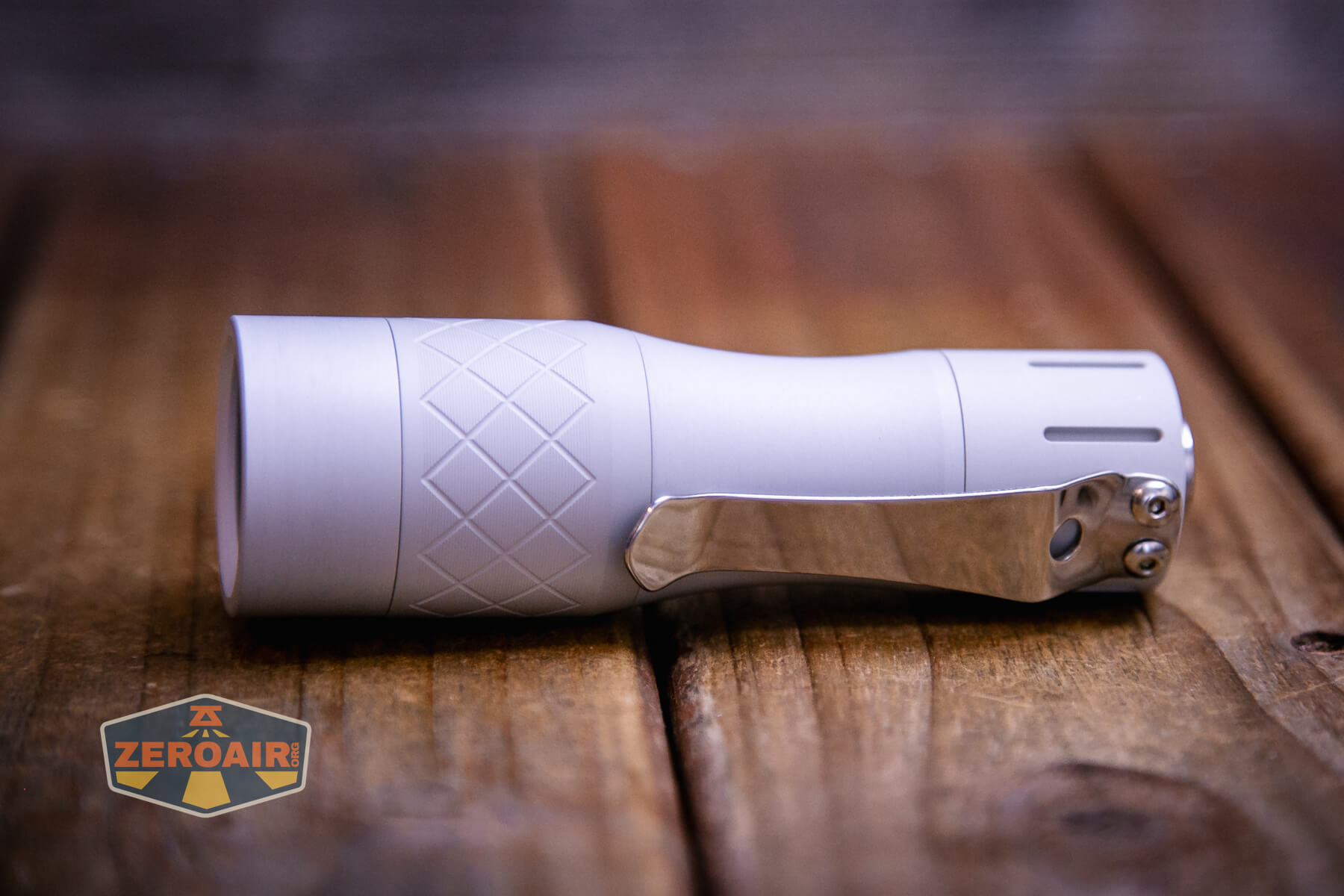 A compact, silver NLightD L3 LEP flashlight with a textured grip and metal clip rests on a wooden surface. A ZeroAir logo is visible in the lower left corner of the image.