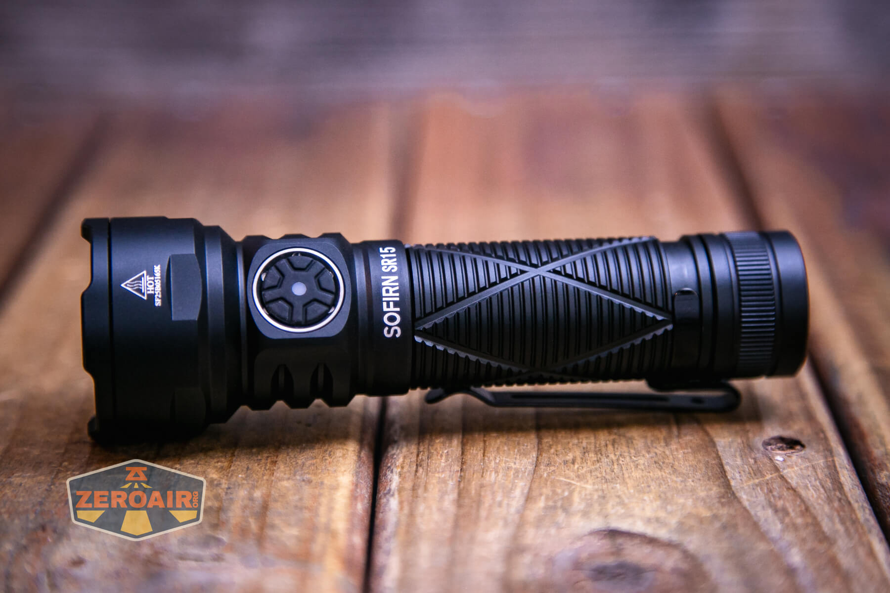 A black Sofirn SR15 rechargeable flashlight with textured grip and side button lies on a wooden surface; a ZeroAir logo is visible in the bottom left corner.