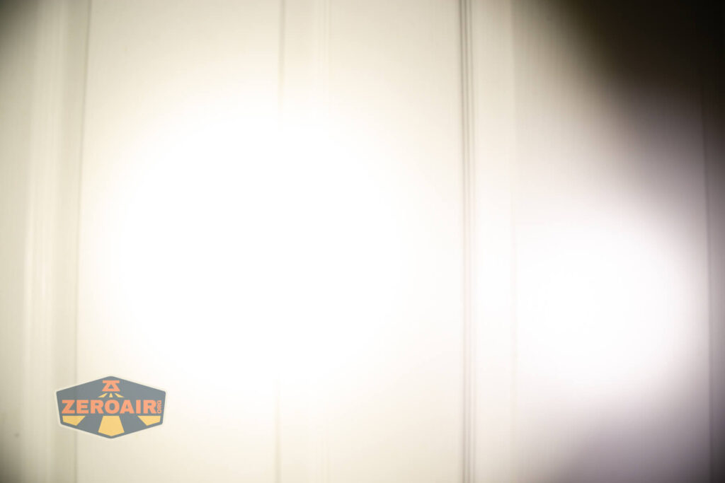 A bright white flashlight beam shines on a white paneled door, creating a central hotspot with blurred edges. The ZeroAir logo is visible in the lower left corner of the image.