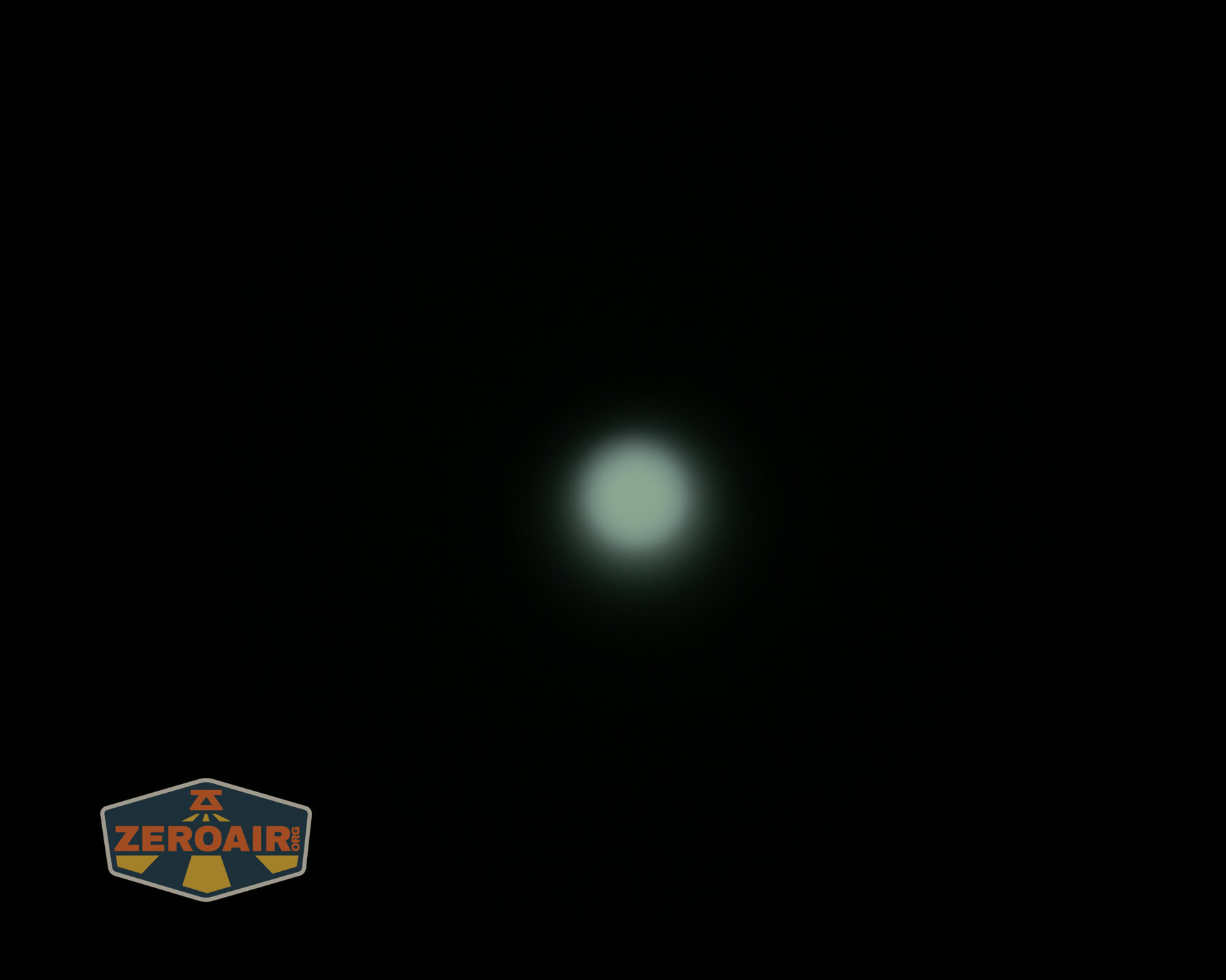 A small, bright white light source is centered against a dark, almost black background. A ZeroAir logo appears in the lower left corner of the image.