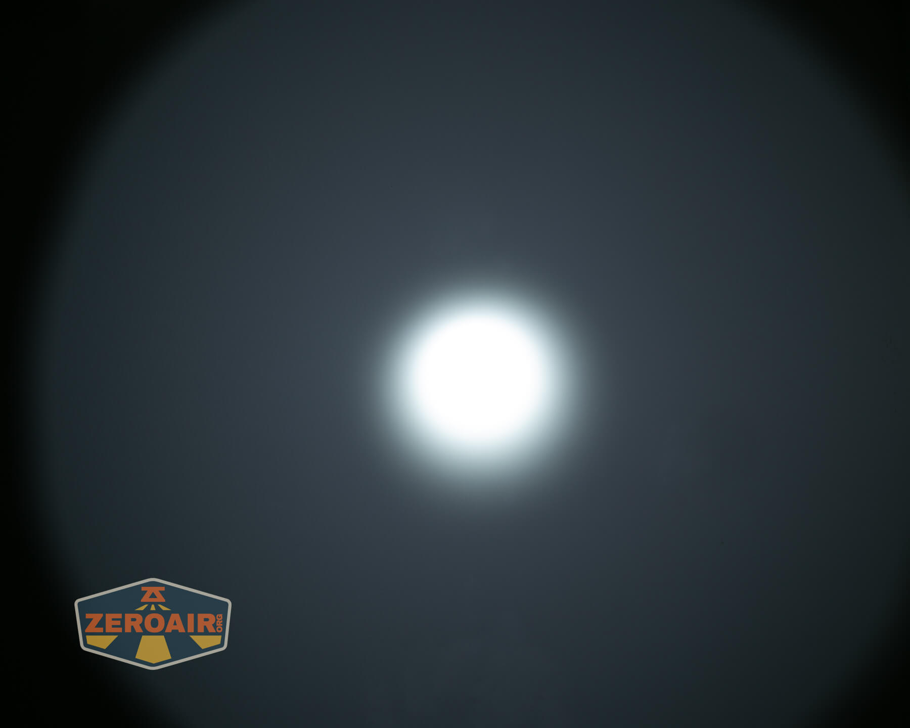A bright, circular white light is centered against a dark, blurred background with a ZeroAir logo in the bottom left corner.