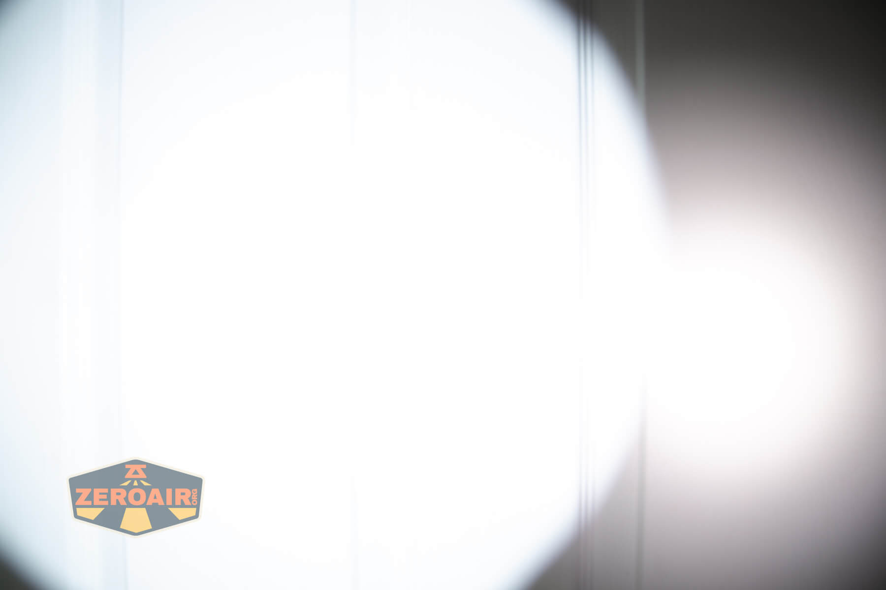 A bright, circular white spotlight shines on a vertical surface, creating a high contrast between the illuminated area and the dim surroundings. The ZeroAir logo is visible in the bottom left corner.