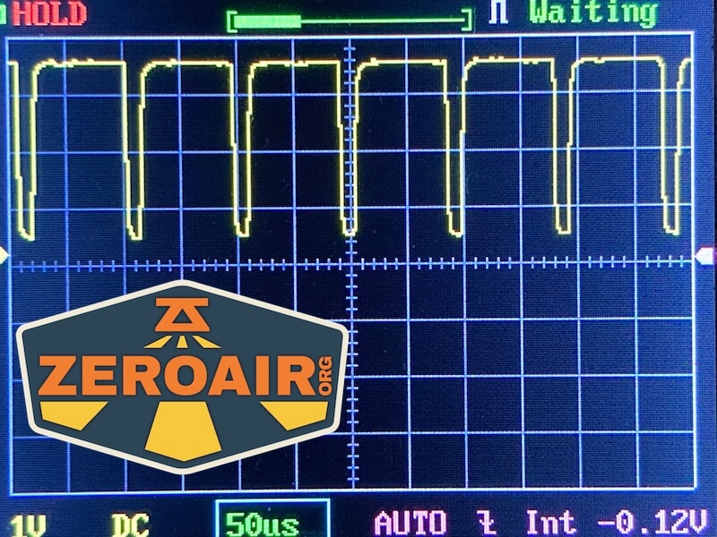 An oscilloscope screen displays a repeating square wave signal. The horizontal scale is set to 50 microseconds per division. A sticker with the Zeroair.org logo is partially covering the lower left corner.