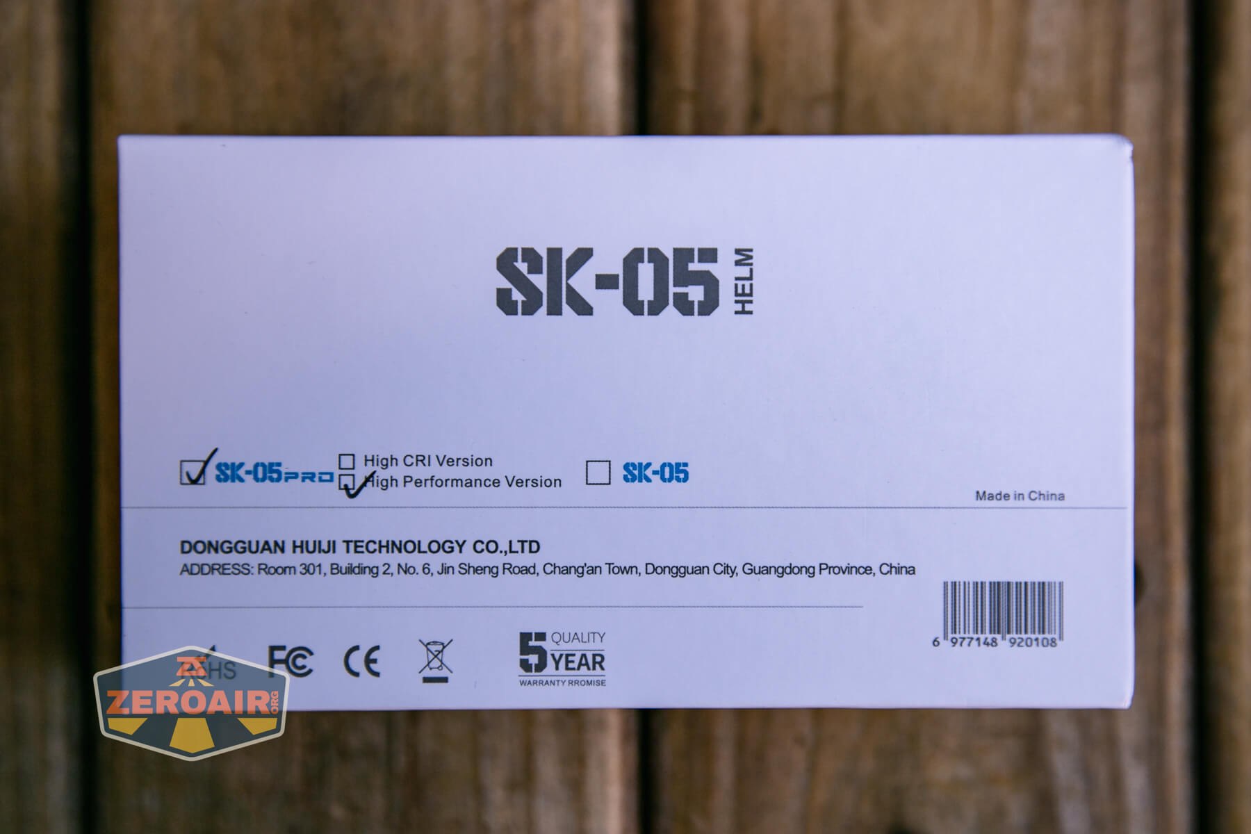 A white product box labeled SK-05 HELM with checkboxes for High CRI Version and High Performance Version, company information, barcode, and various certification icons, set on a wooden surface.