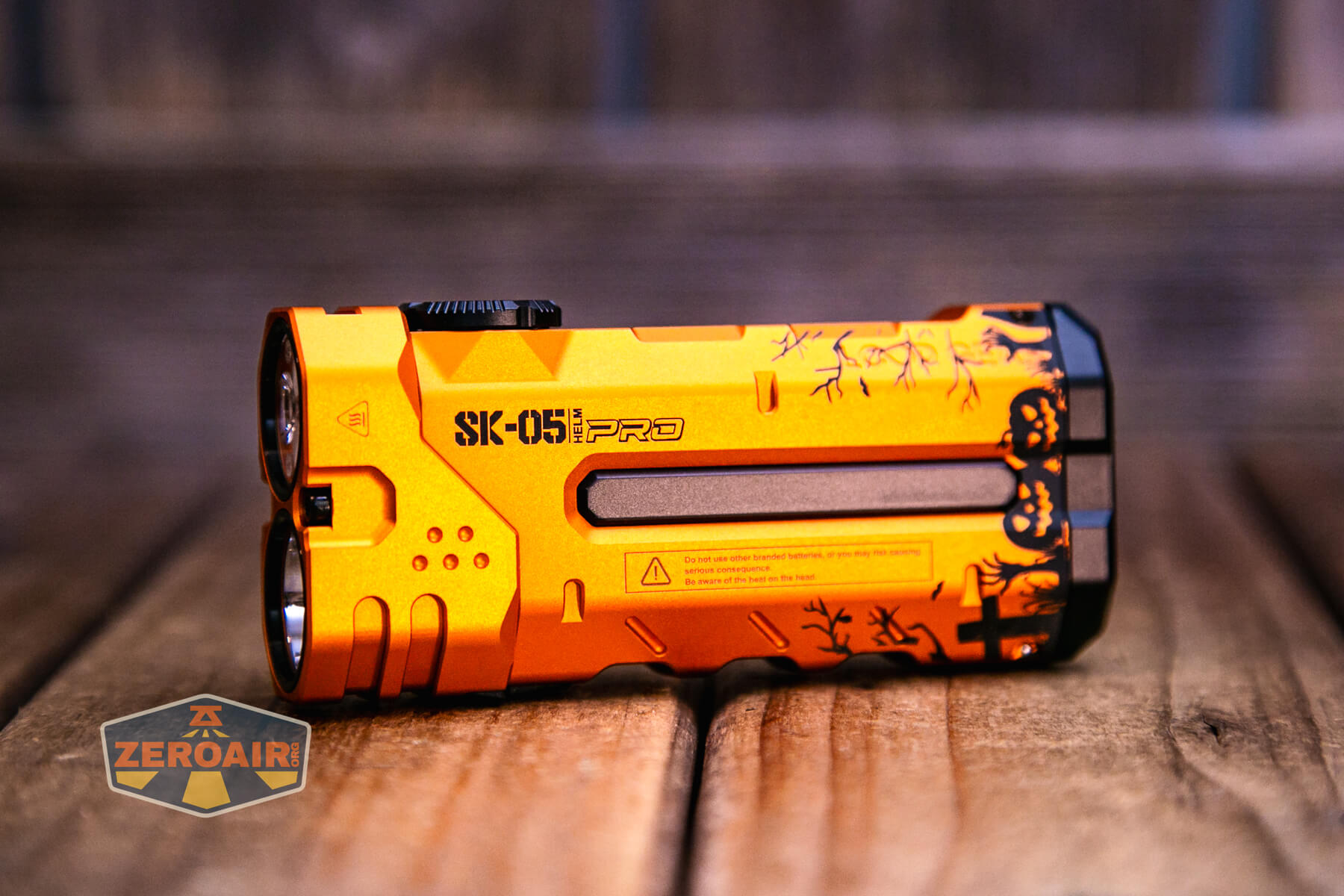 An orange SK-051 PRO flashlight with black accents and printed designs rests on a wooden surface. The ZER0AIR logo appears in the lower left corner of the image.