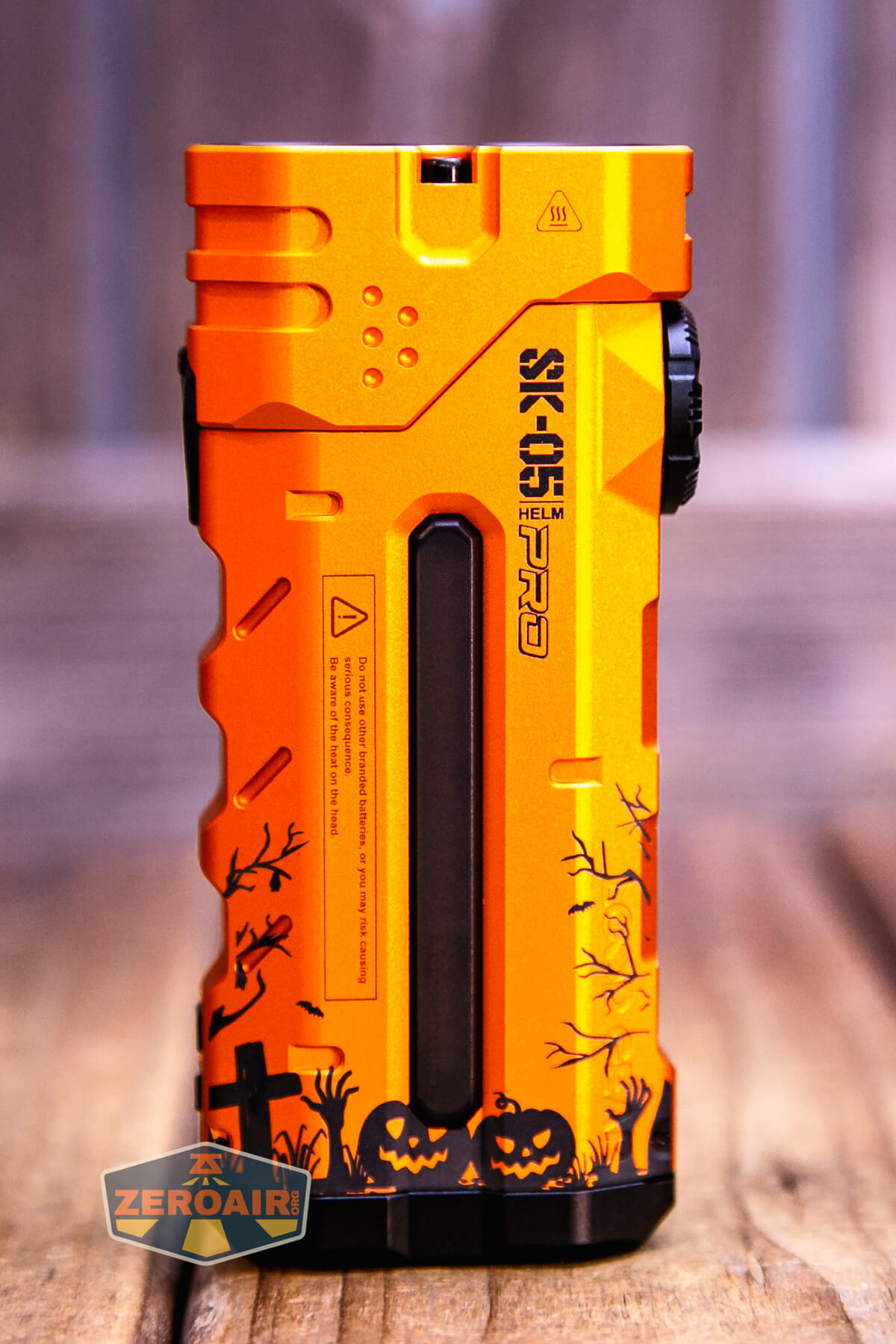 An orange flashlight with black Halloween-themed designs, including pumpkins and gravestones, and labeled “SK01 HELM.” The background is wooden, and there is a ZEROAIR logo in the bottom left corner.