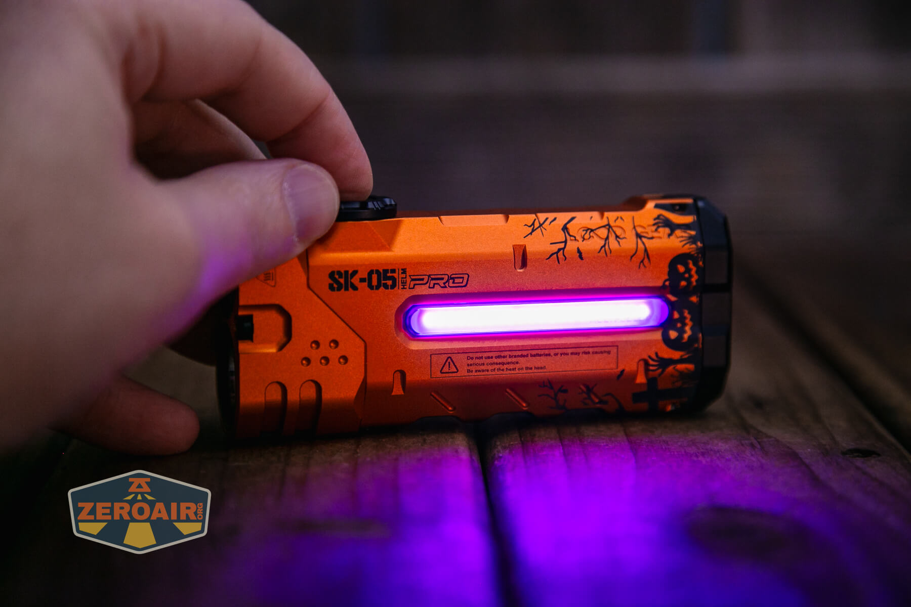 A hand holds an orange SK-051 PRO device with a glowing purple light strip. The device has black patterns, a display, and buttons, resting on a wooden surface with a ZeroAir logo visible in the corner.