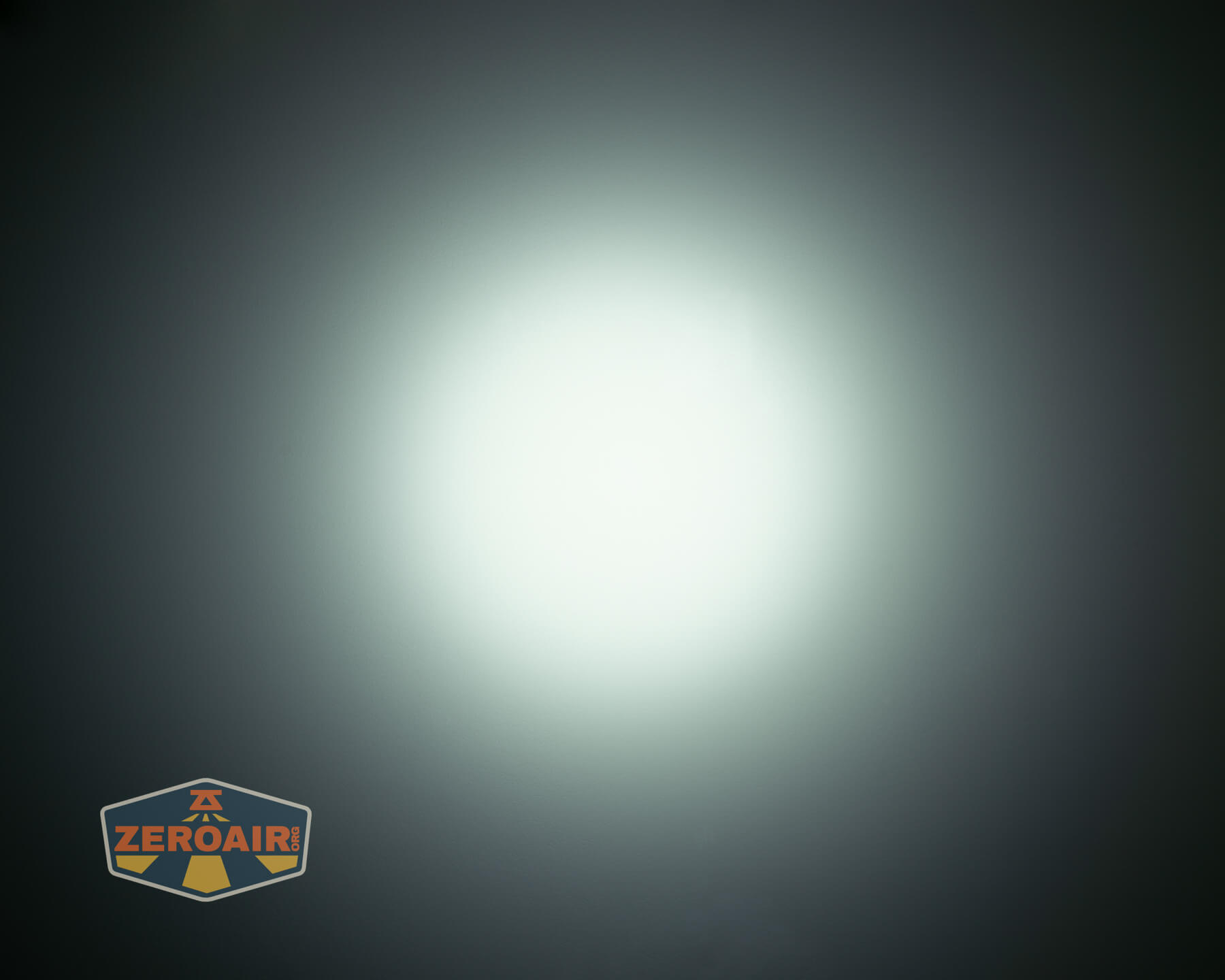 A bright, circular white light beam shines in the center of a dark background. The logo “ZEROAIR” appears in the bottom left corner.